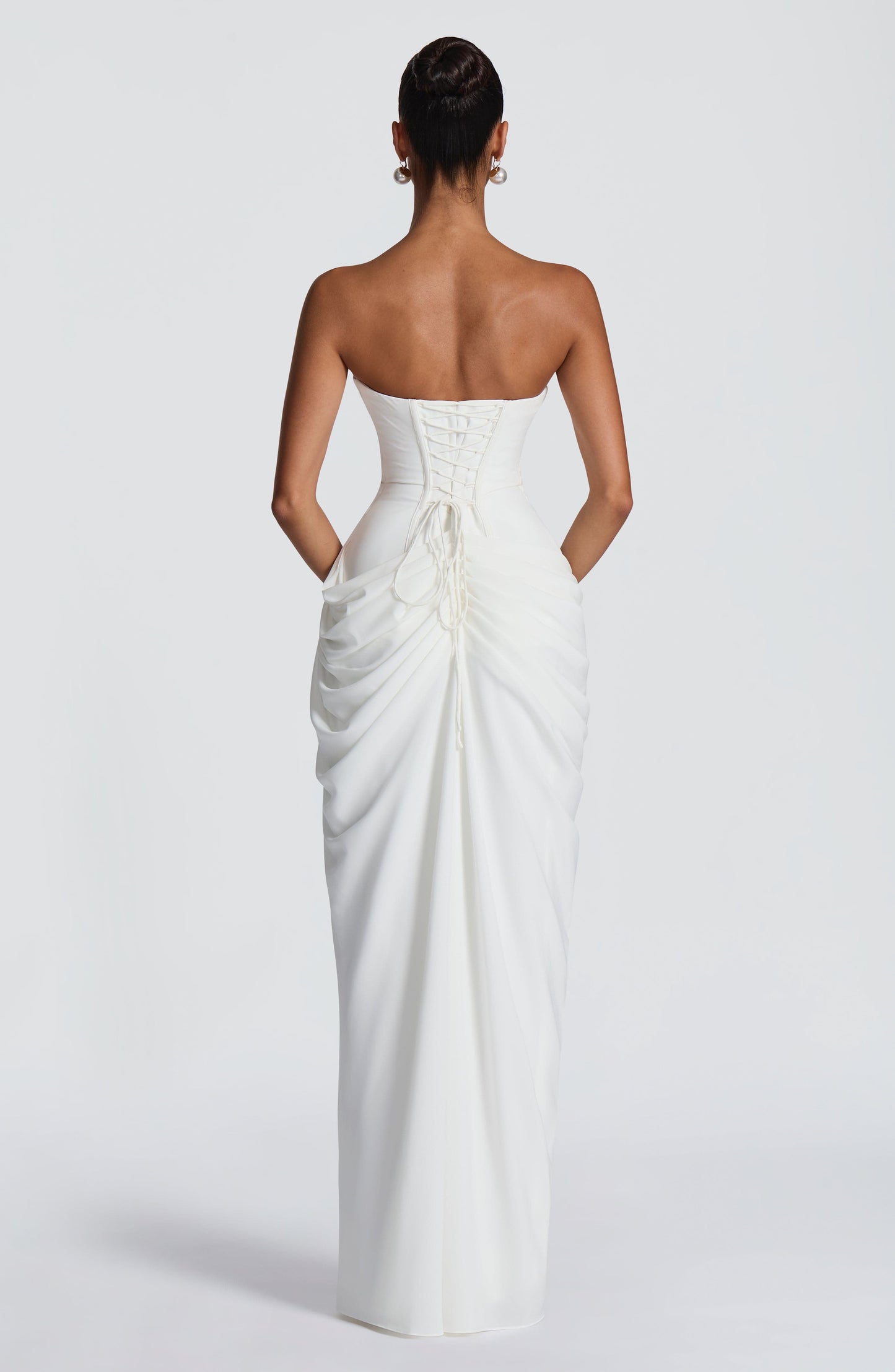 Back view of white strapless maxi dress with lace-up corset detail and draped skirt
