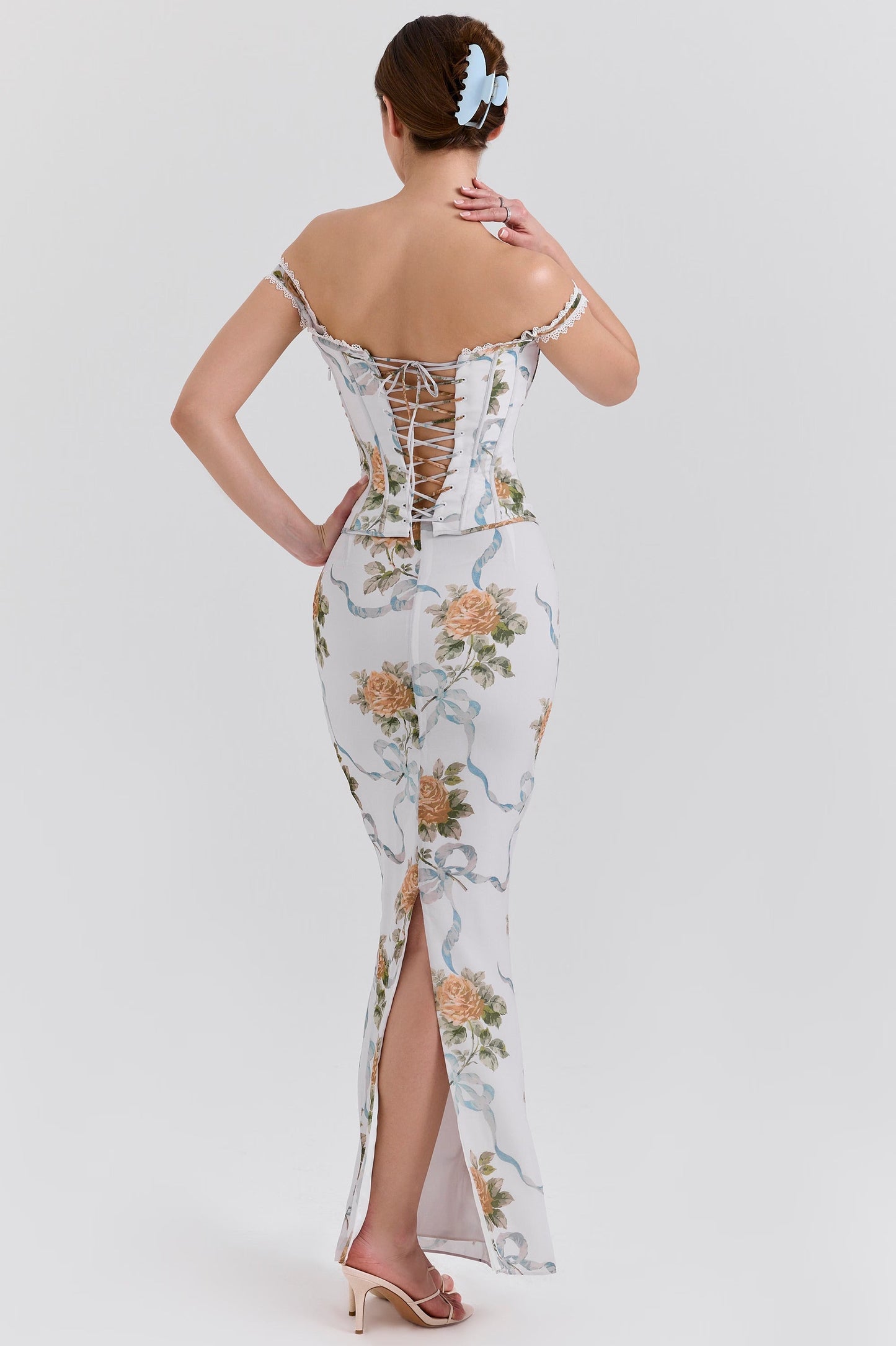 Back view of a white off-shoulder corset floral maxi dress, showing the lace-up detail on the bodice and a subtle slit.