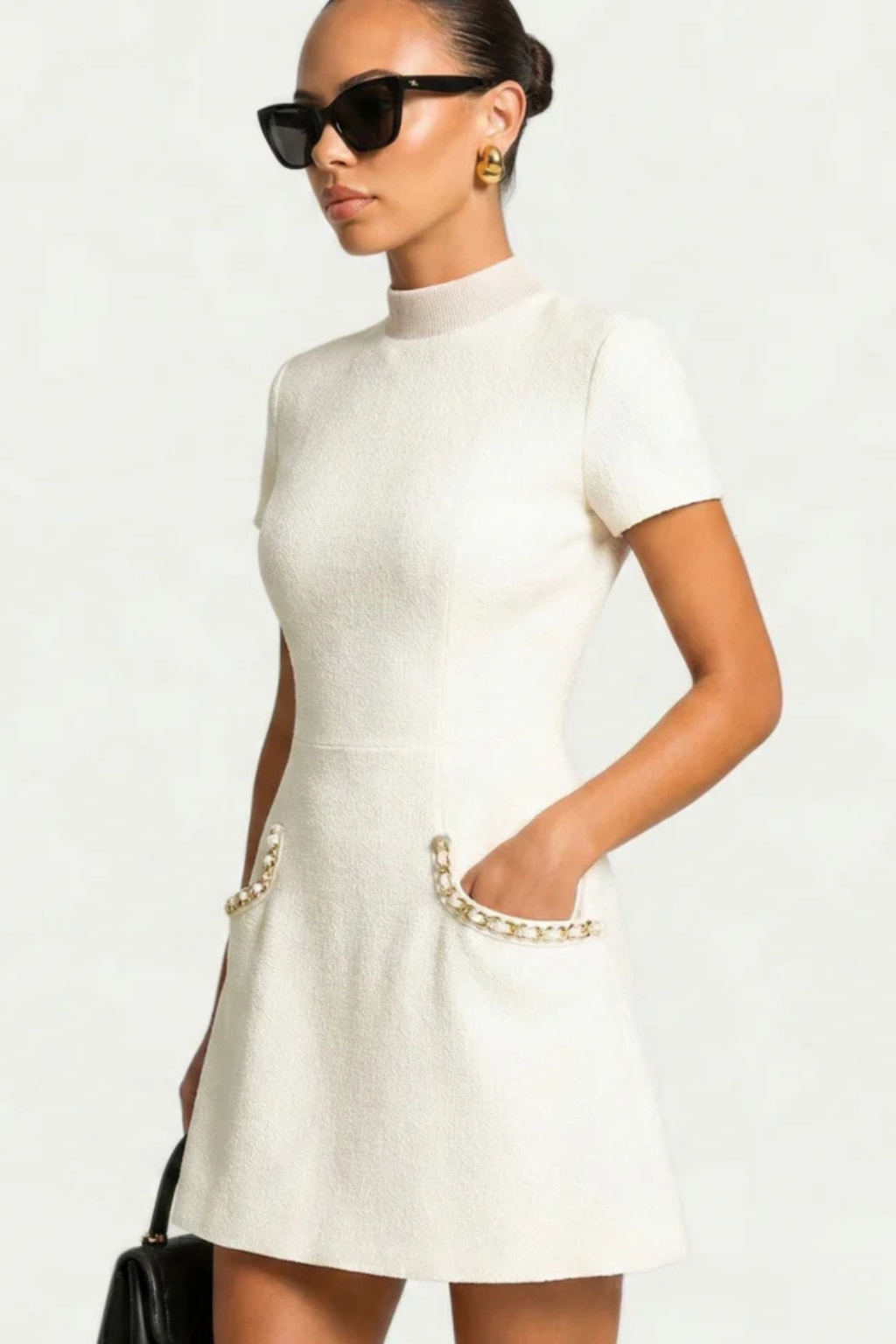 Angled view of white pearl trim mock neck mini dress, featuring short sleeves and detailed pockets.