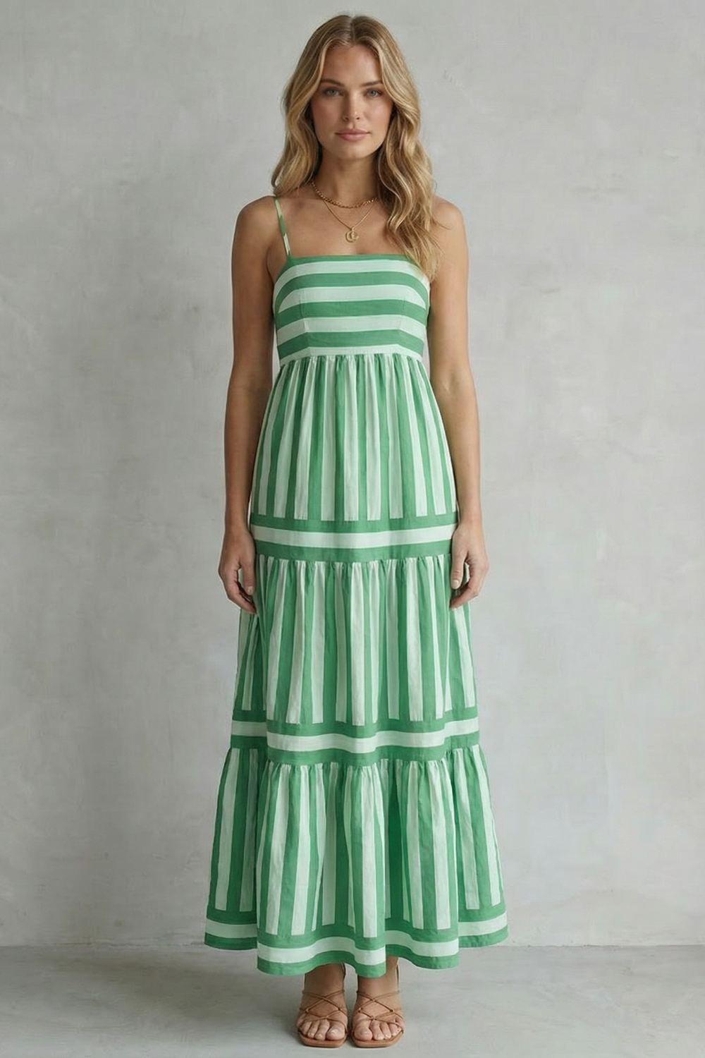 Full-length view of a woman wearing a green and white striped strappy tiered maxi dress, showcasing the flowy design.