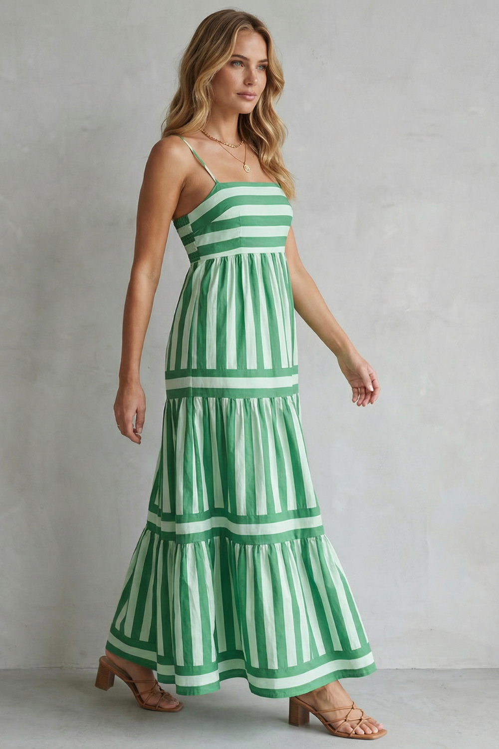 Side profile of a woman in a green and white striped tiered maxi dress, highlighting the elegant movement of the skirt.