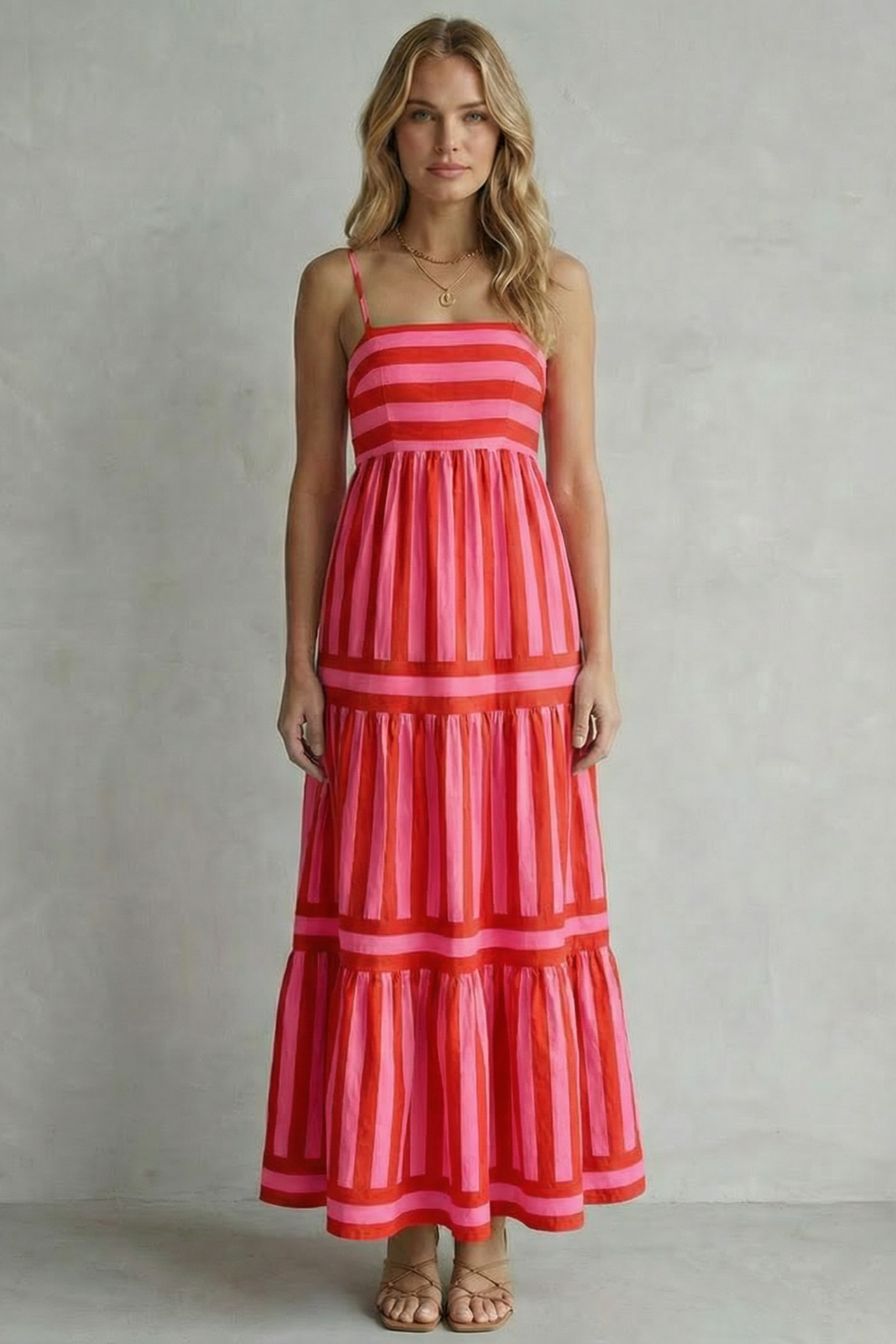 Full-length image of a woman wearing a red and pink striped strappy tiered maxi dress, showing the full length.