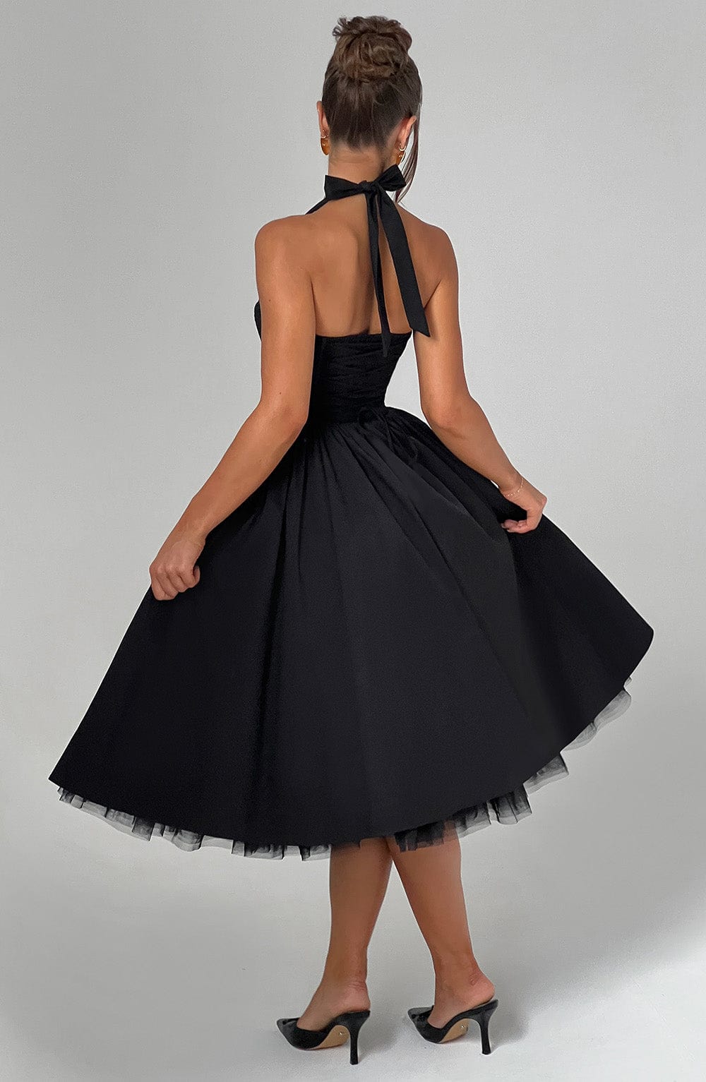 Back view of a black backless halter neck midi dress, showcasing the tie-neck detail and the full, twirling skirt.