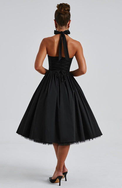 Back view of a black backless halter neck midi dress with a tied bow and cinched corset-style waist.