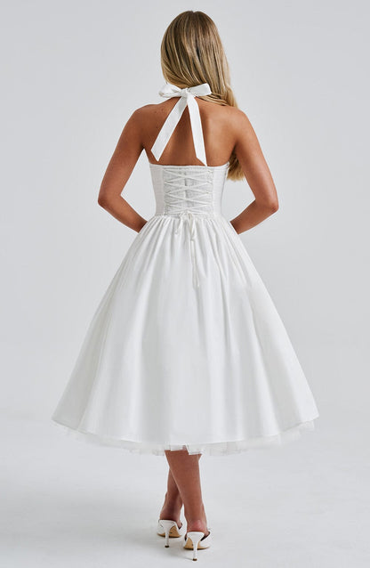 Back view of a white backless halter neck midi dress with a lace-up corset detail and tie closure at the neck.