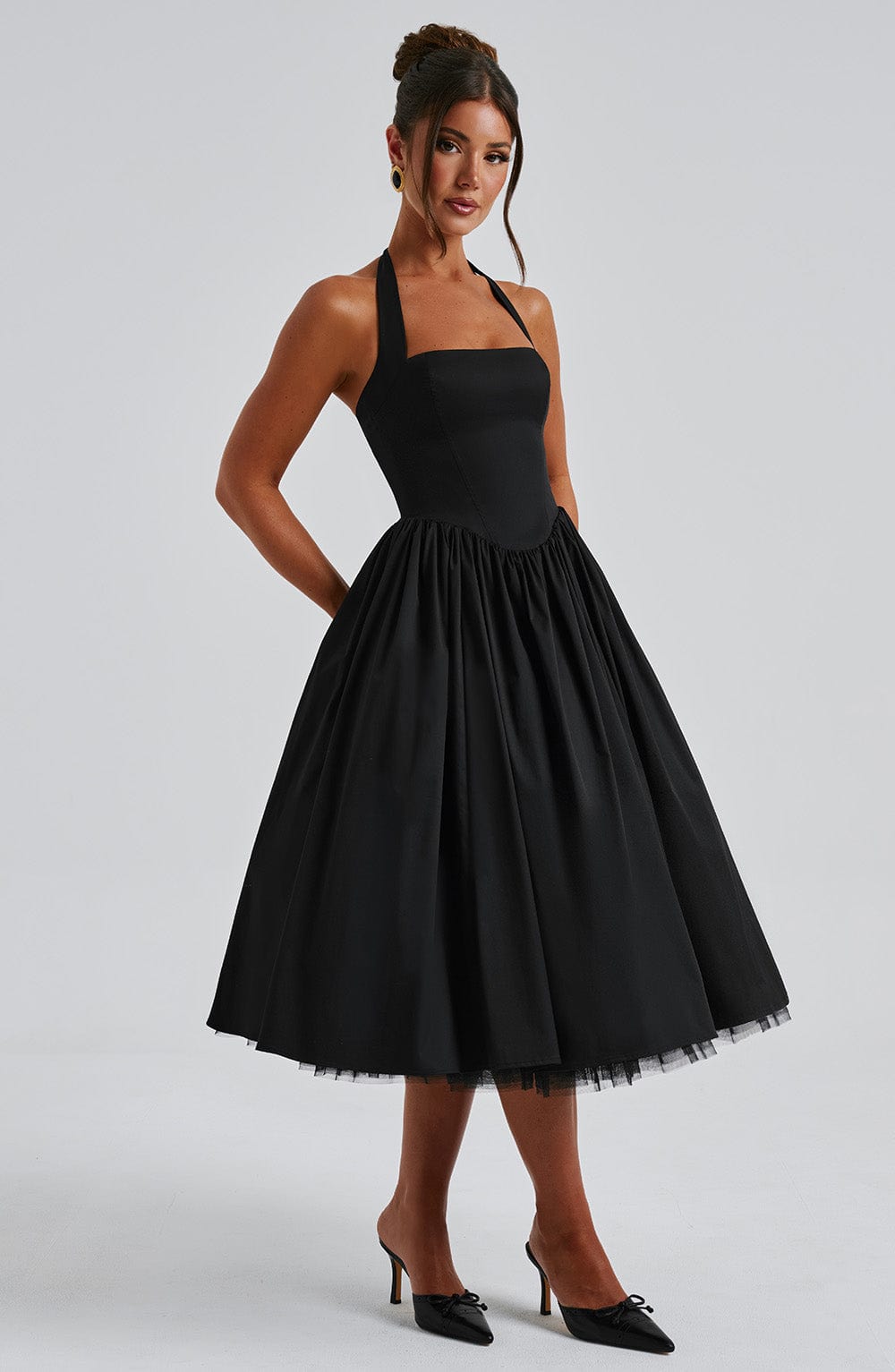Side view of a black backless halter neck midi dress, highlighting the elegant silhouette and flowing skirt movement.