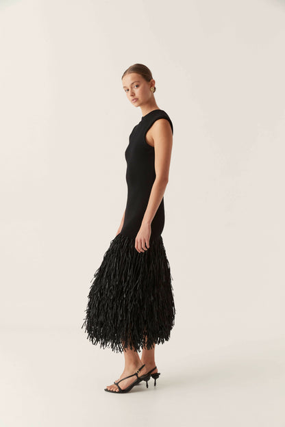 Side profile of a black bodycon maxi dress with a fringed hem and a sleeveless cut, a chic vacation dress option.