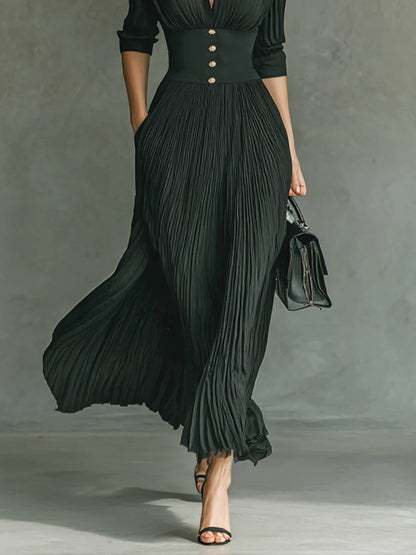 Lower half detail of black pleated maxi dress skirt showing high fitted waist and swaying hemline