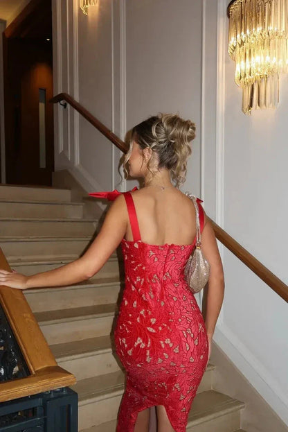 Back view of a woman walking up stairs in a red bow shoulder lace bodycon maxi dress, highlighting the fitted silhouette and lace details.