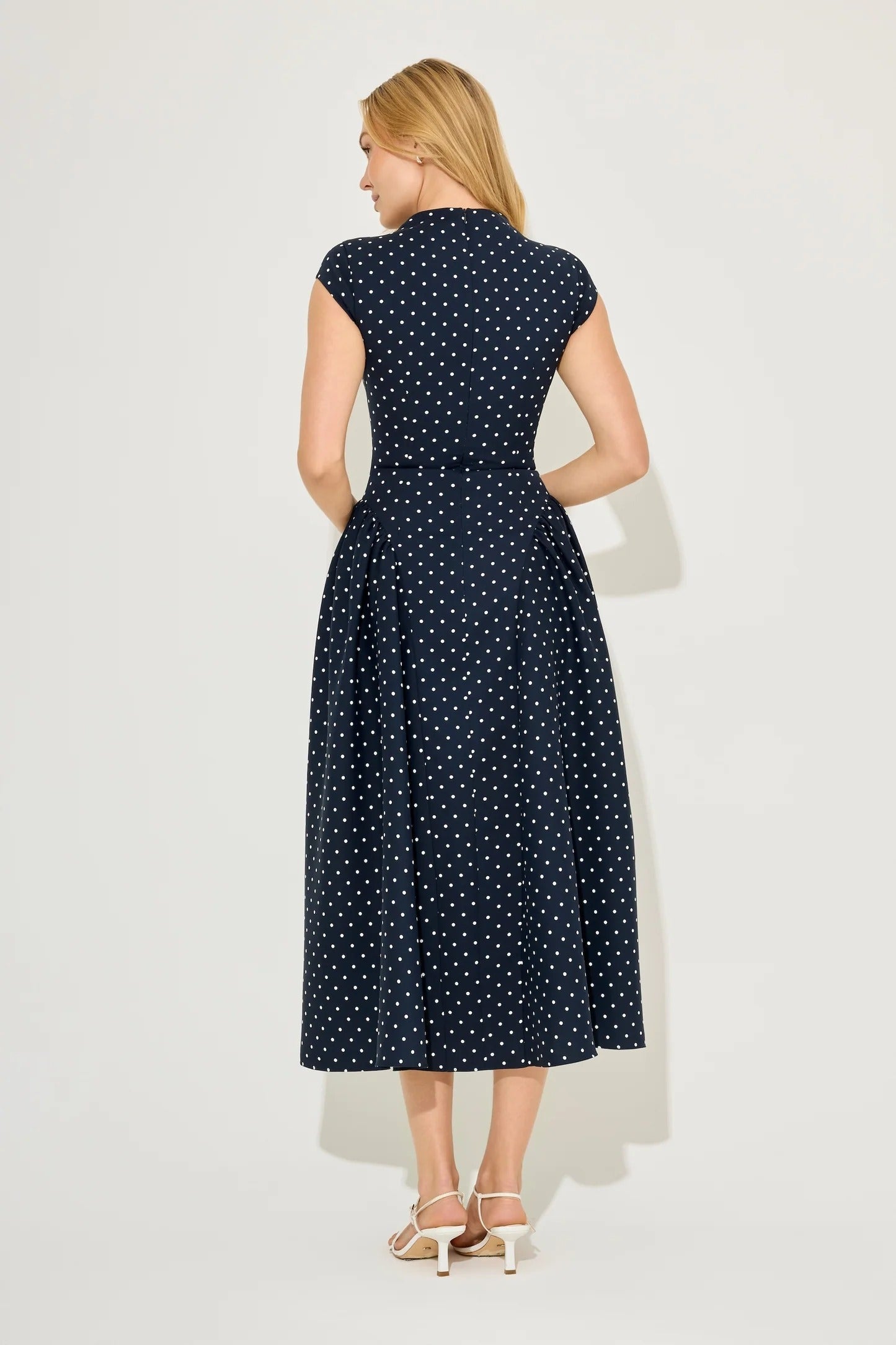 Back view of navy polka dot cap sleeve midi dress with gathered skirt and fitted bodice seams