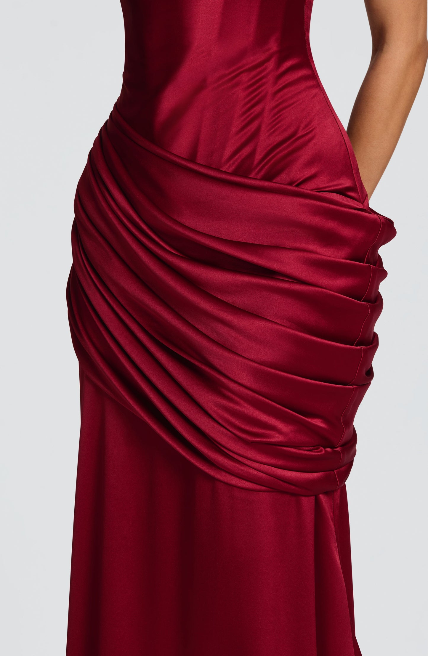 Detail of burgundy satin maxi dress ruched wrap overlay at hips with smooth skirt fabric