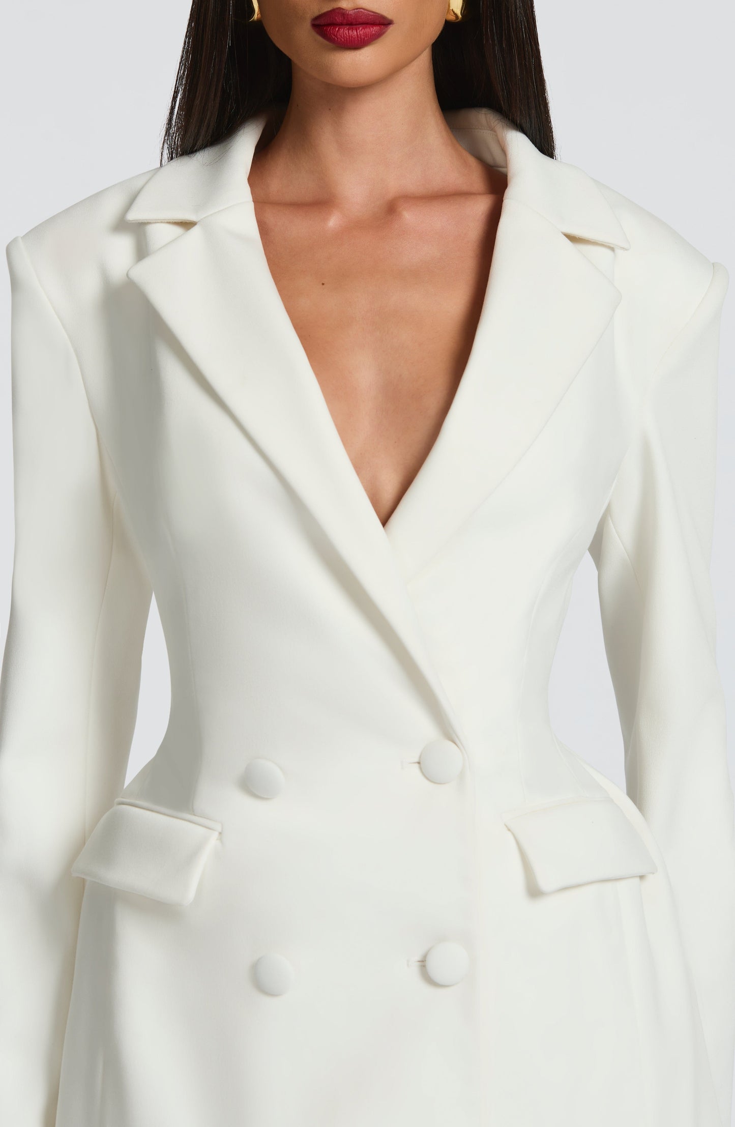 Close-up of the bodice of a white double-breasted mini dress, showing the lapels, deep V-neck, and four white buttons.