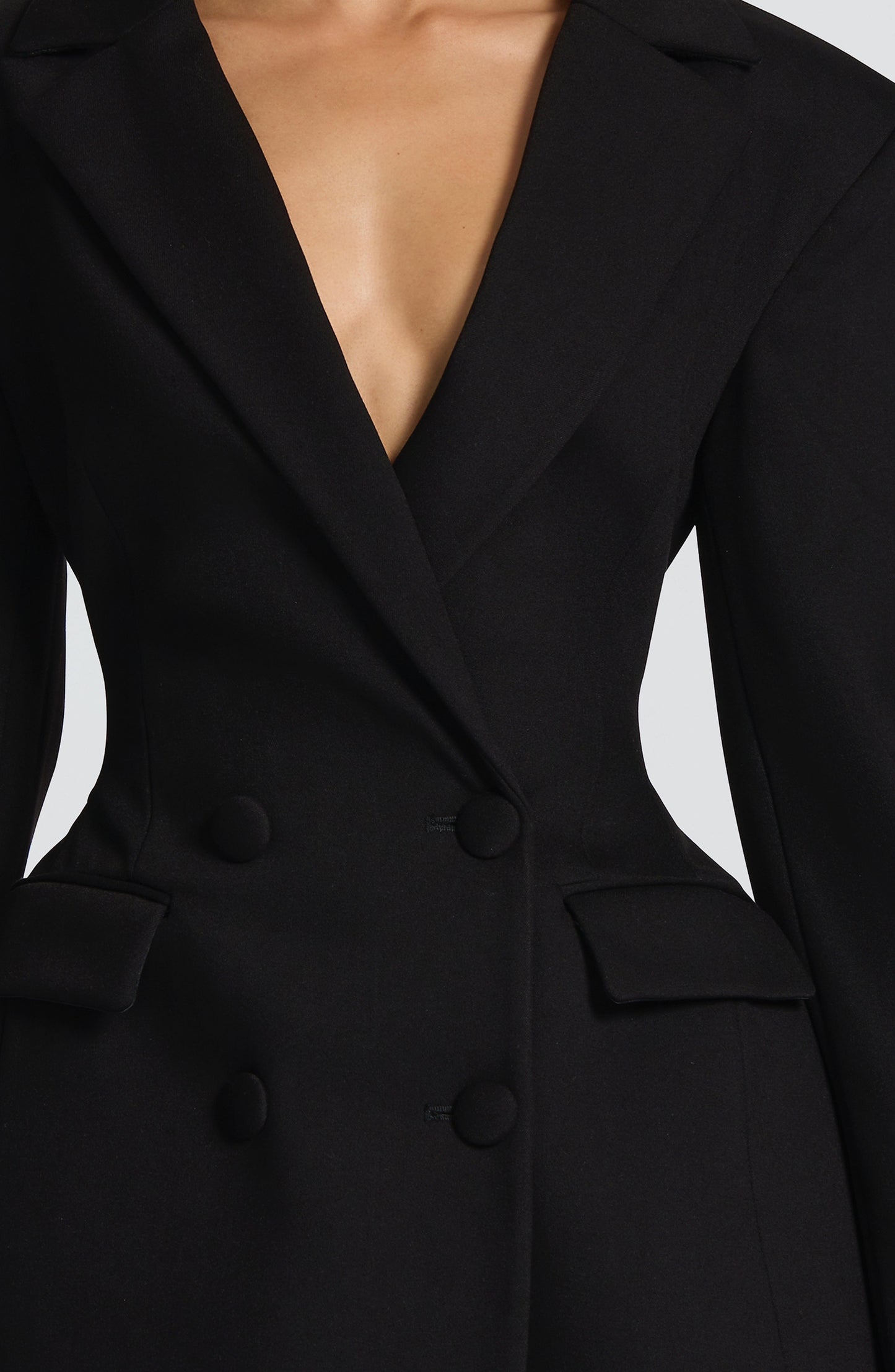Close-up of the black double-breasted mini dress, showing the lapels, deep V-neckline, and four black buttons.