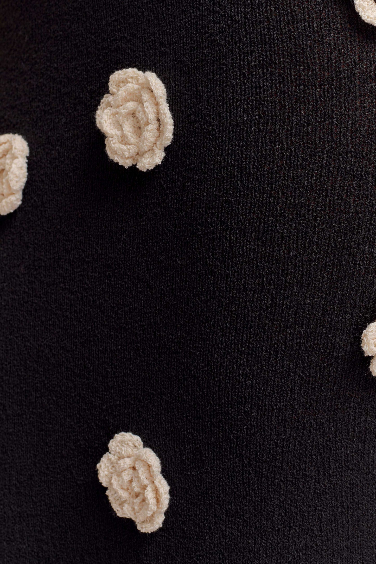 Detailed close-up of the white floral crochet appliques on the black knit maxi dress fabric