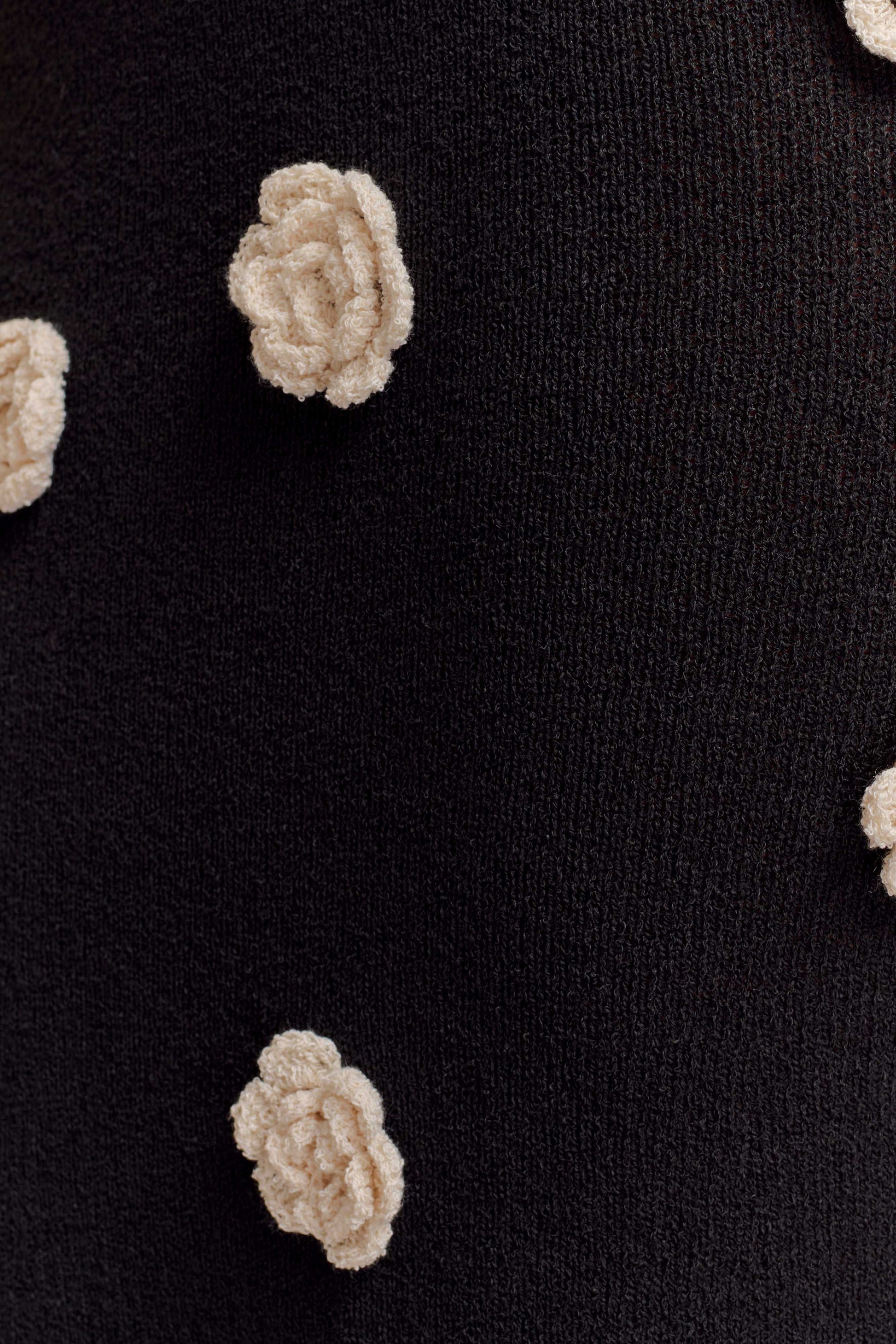 Detailed close-up of the white floral crochet appliques on the black knit maxi dress fabric