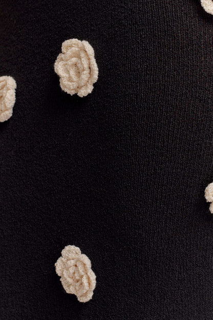 Detailed close-up of the white floral crochet appliques on the black knit maxi dress fabric