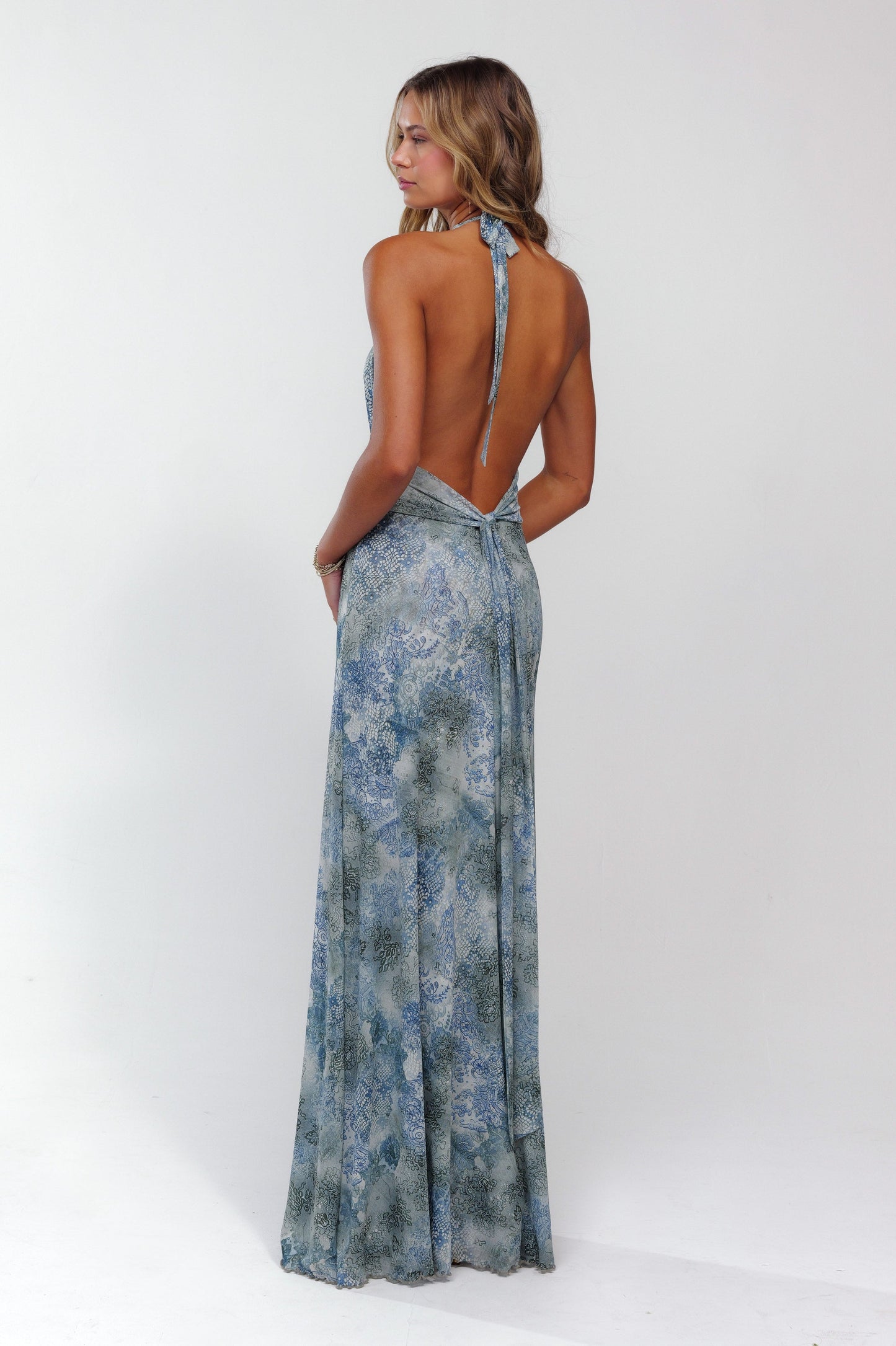 Back view of a women's blue patterned halter maxi dress, showcasing the open back and tie closure.