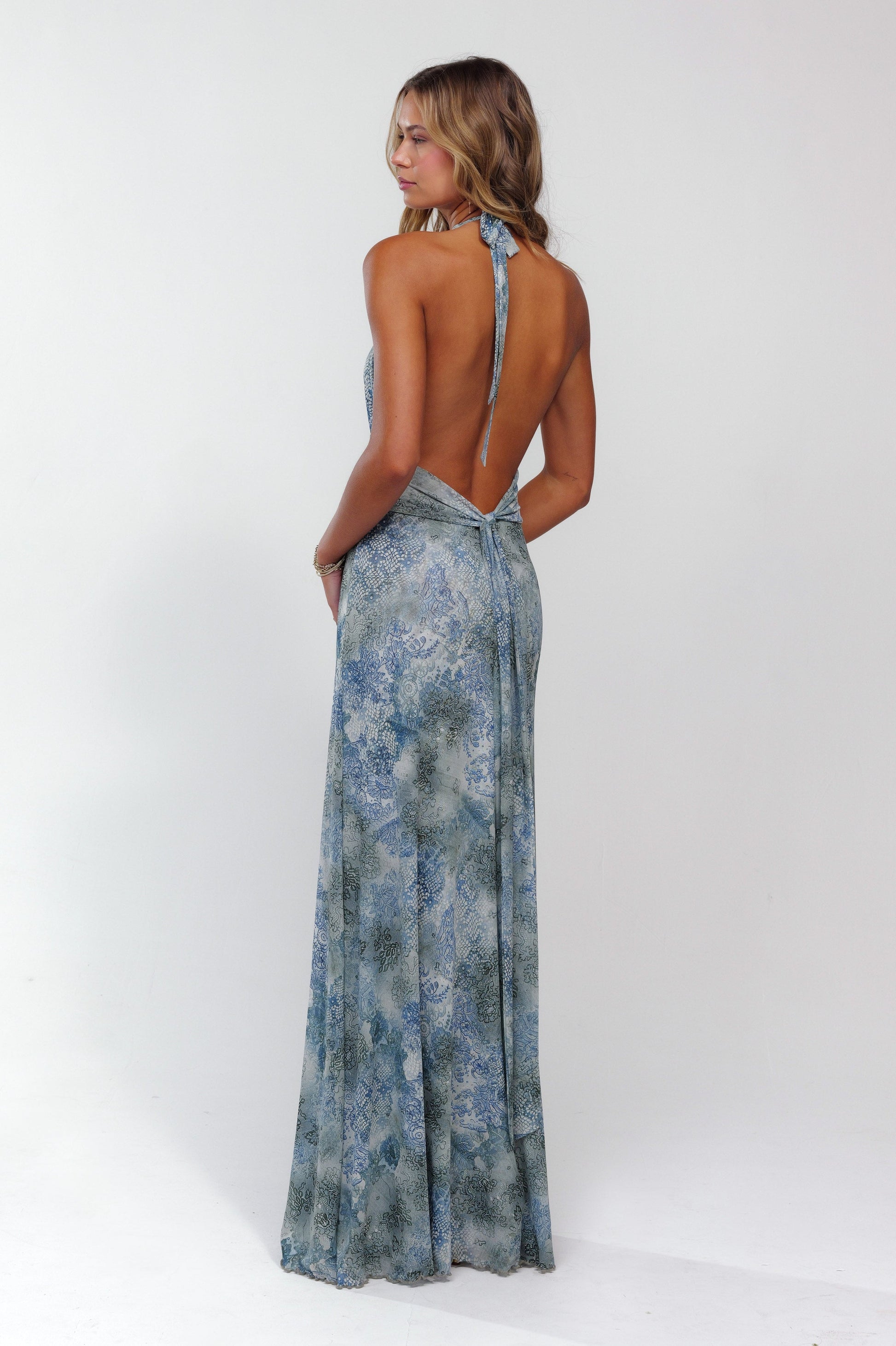 Back view of a women's blue patterned halter maxi dress, showcasing the open back and tie closure.
