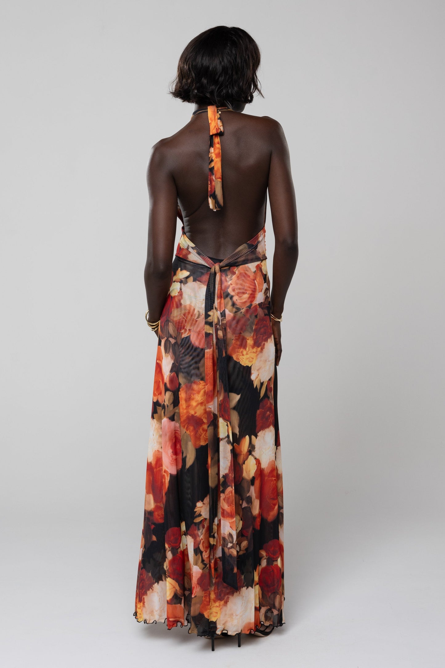 Back view of the floral halter maxi dress in orange and red, highlighting the tie-neck detail and open back design, an elegant dress for wedding guests.