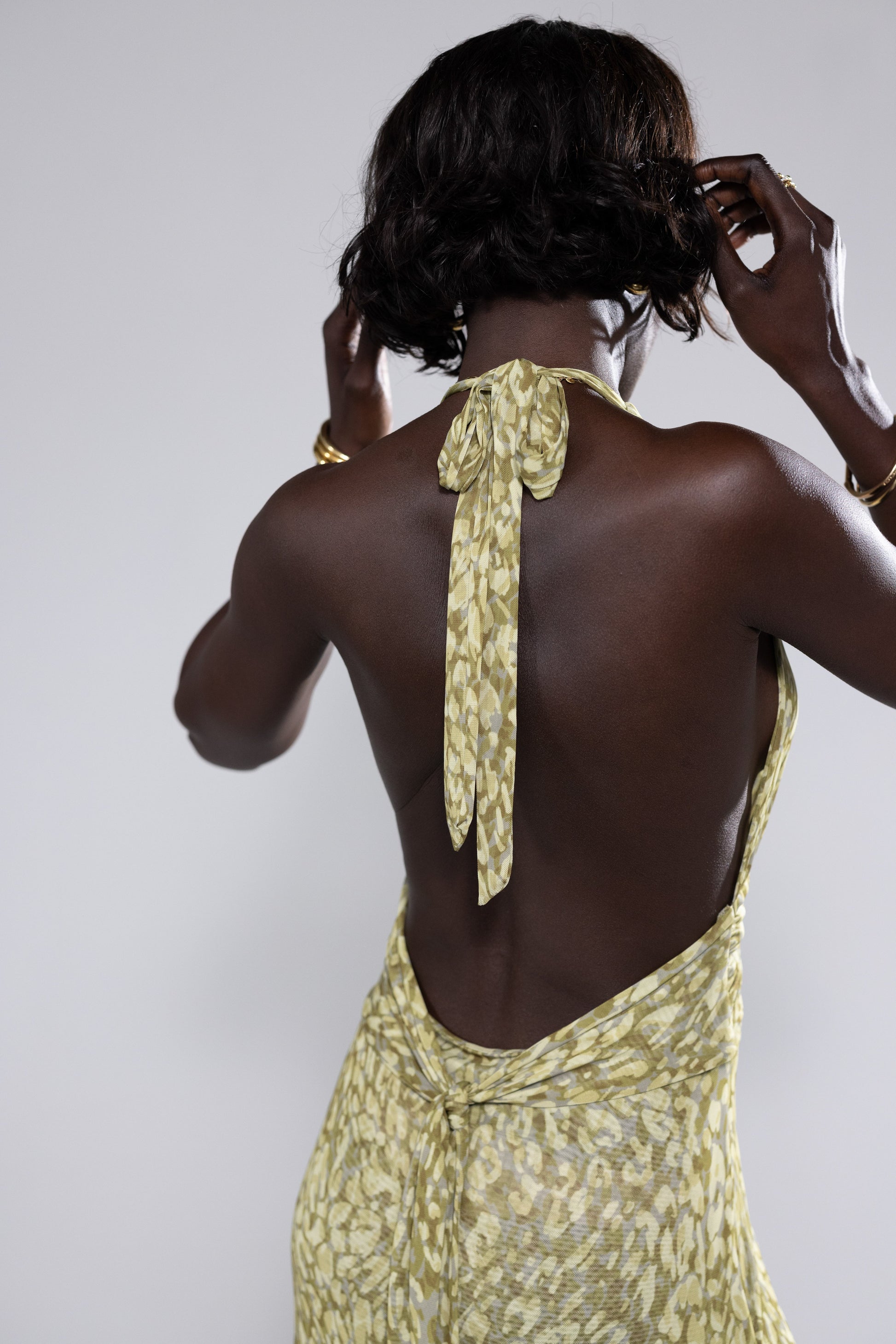 Back view of the green and yellow abstract print halter maxi dress, showcasing the tie-neck closure and open back, an elegant option for wedding guests.
