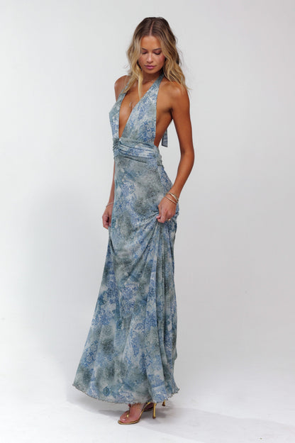 Side profile of a women's blue patterned halter maxi dress, showing the flowing skirt and elegant design.
