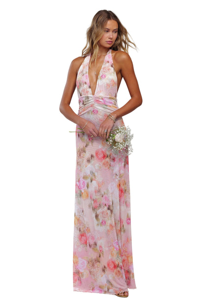 Front view of a women's floral halter maxi dress in pink with a deep V-neck and ruched waist, holding flowers.