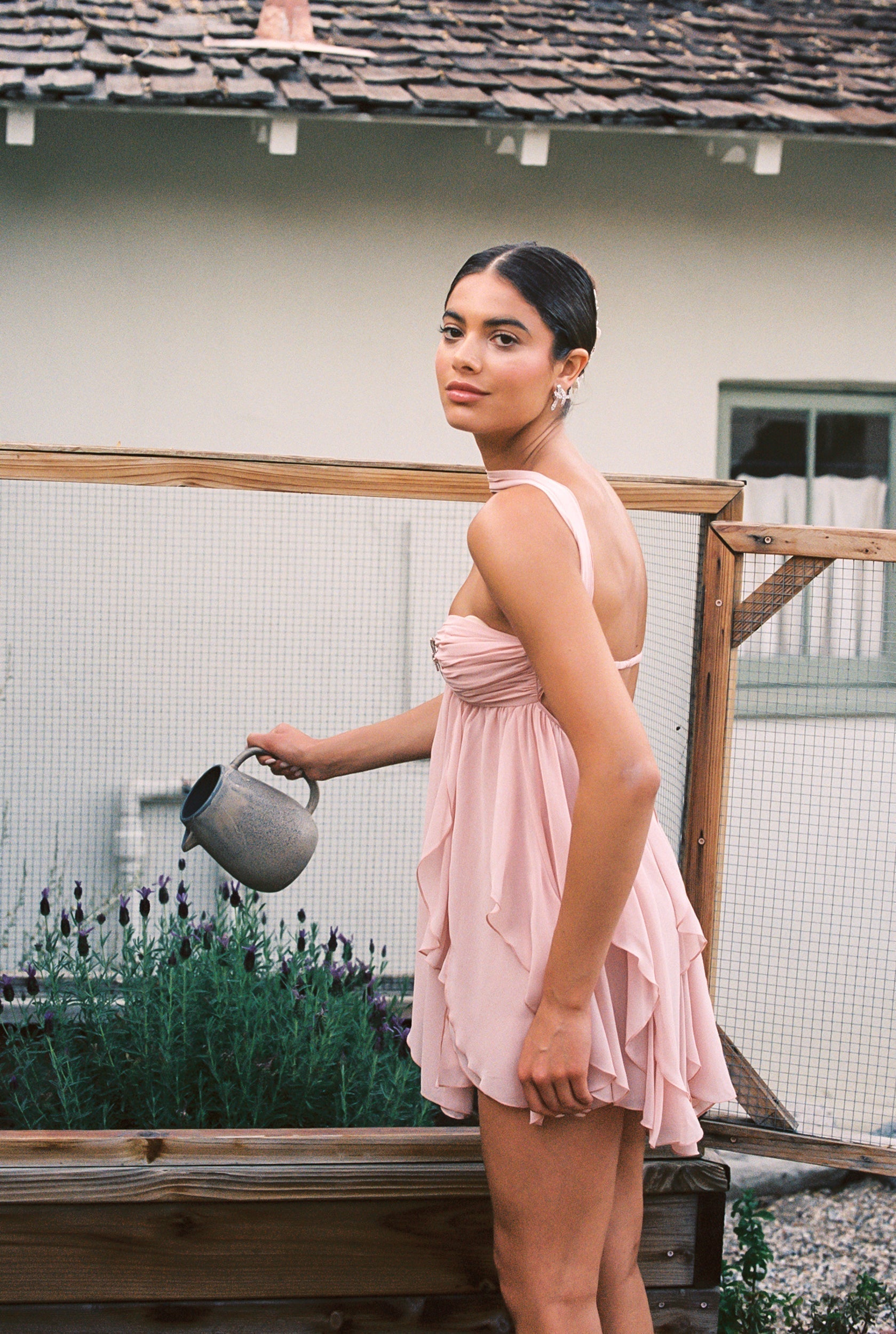 Side view of women's pink halter neck tiered mini dress with a star brooch, showing the ruffled skirt and back detail.