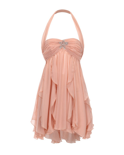 Studio shot of women's pink halter neck tiered mini dress with a star brooch on the ruched bust and a ruffled skirt.