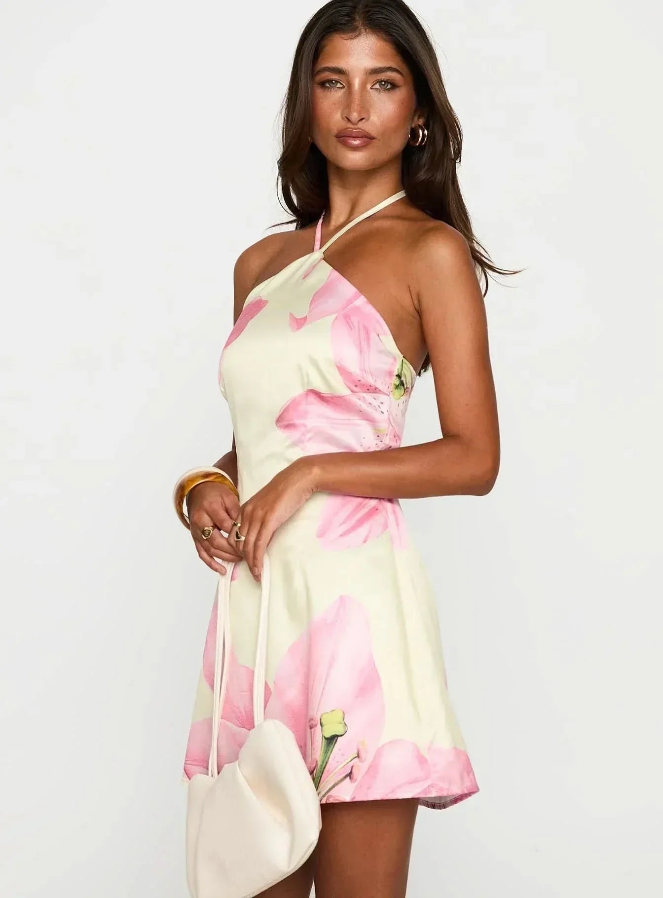 Women light yellow and pink floral mini dress with halter neckline and satin finish, holding a white bag