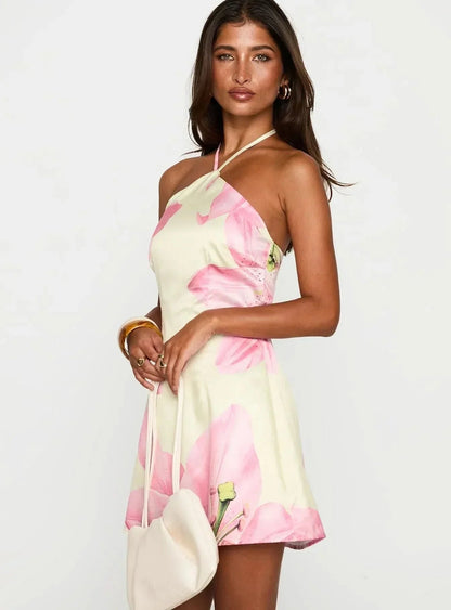 Women light yellow and pink floral mini dress with halter neckline and satin finish, holding a white bag
