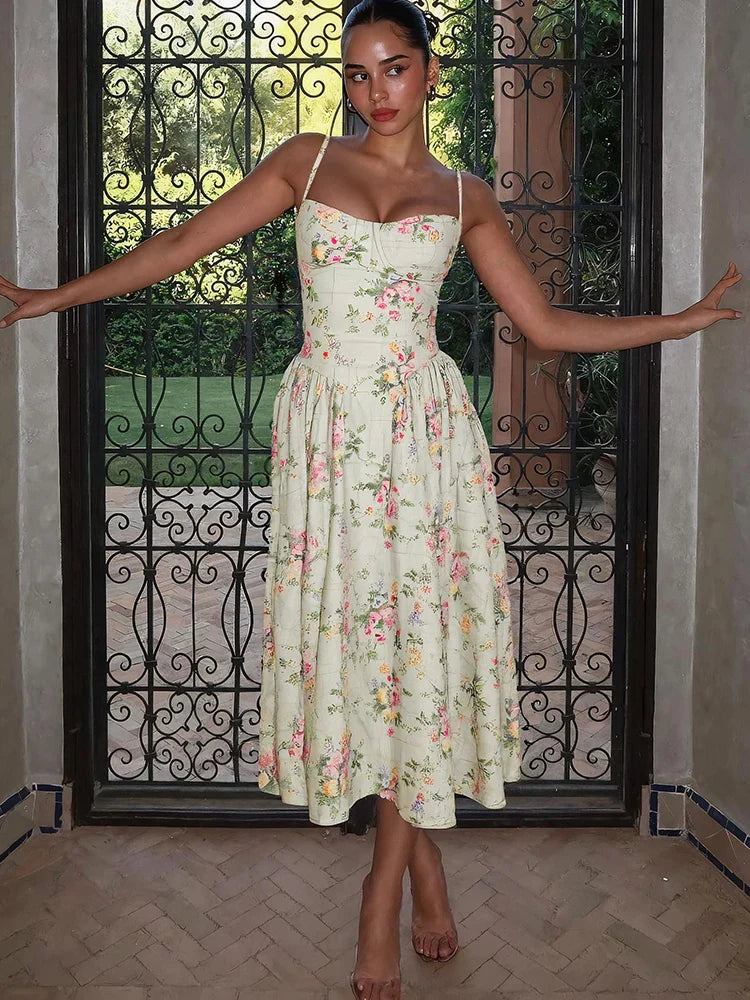 Woman posing in a light green floral sweetheart neck midi dress with a pleated skirt, in front of an ornate gate.