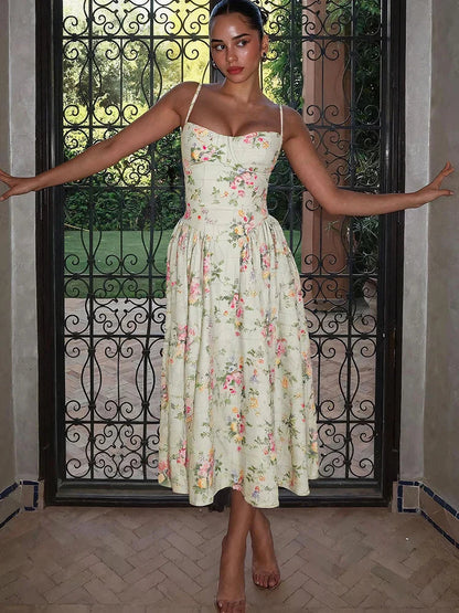 Woman posing in a light green floral sweetheart neck midi dress with a pleated skirt, in front of an ornate gate.