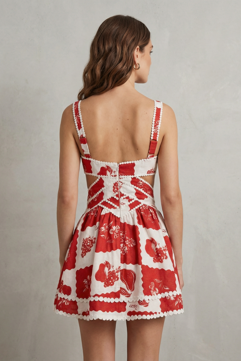 Back view of a women's red and white floral mini dress, showing the crisscross waist detail and scalloped trim on the straps.