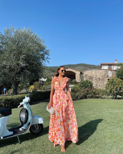 Women's summer floral V-neck maxi dress in orange and pink, with ruffled shoulder details and waist cutouts, next to a vintage scooter.