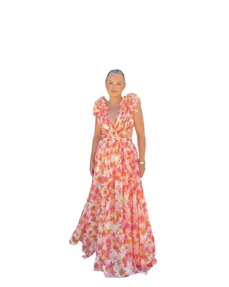 Women's summer floral V-neck maxi dress in orange and pink, with ruffled shoulder details and waist cutouts, standing in a garden.