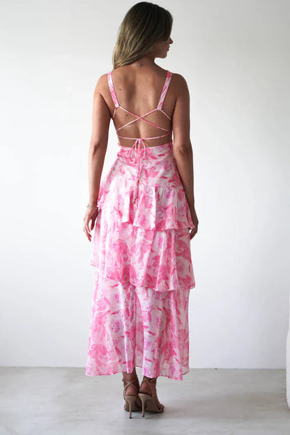 Back view of a women's pink floral V-neck tiered maxi dress, showing criss-cross strap details and a full tiered skirt.