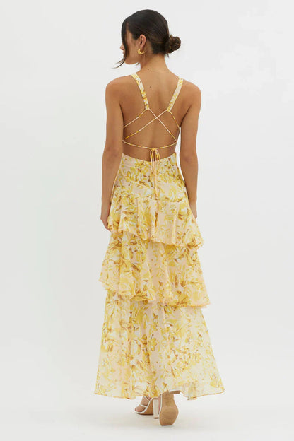 Back view of a yellow floral v-neck tiered maxi dress, showing the criss-cross strap detail and open back design.