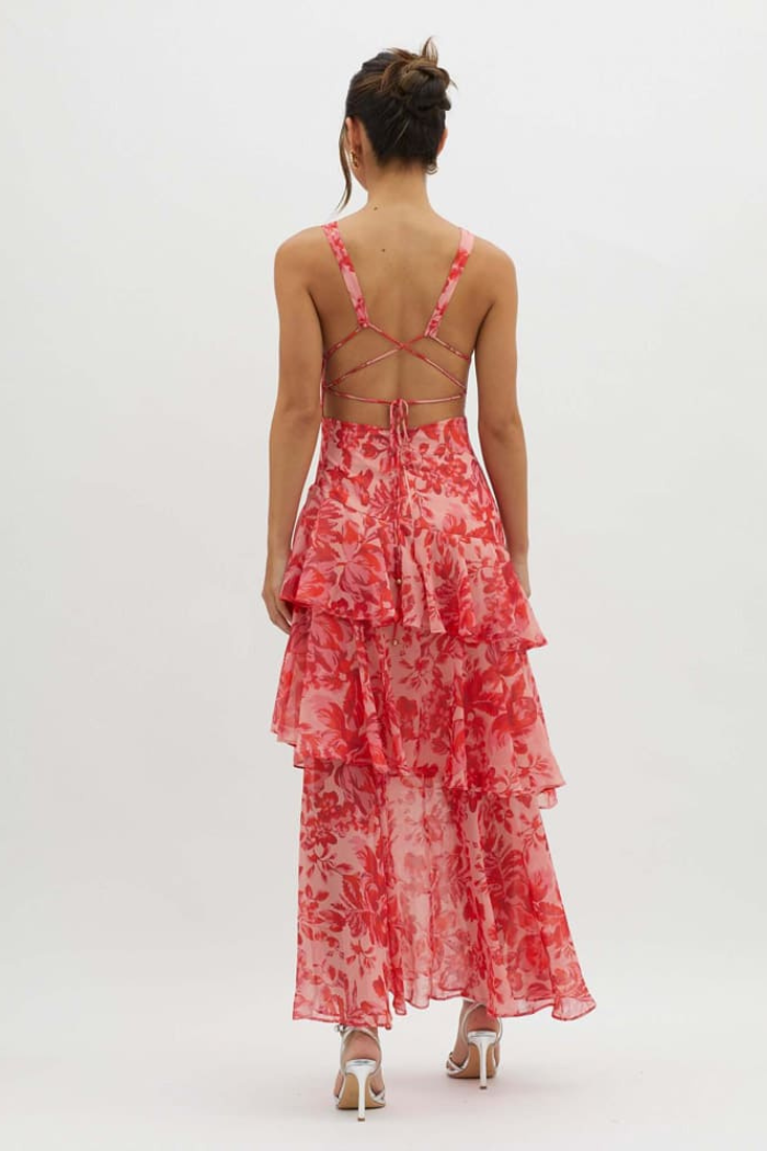 Rear view of a women's pink floral v-neck tiered maxi dress, displaying the full tiered skirt and intricate back strap design.