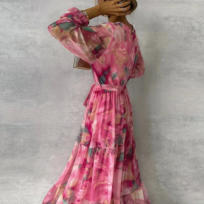 Back view of pink watercolor floral maxi dress with long sheer sleeves, tie belt, and tiered skirt