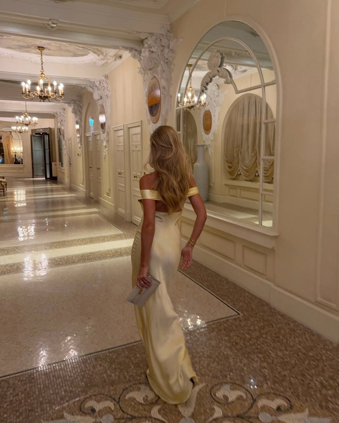 Back view of a woman walking in a flowing light yellow satin maxi dress, highlighting the elegant drape.
