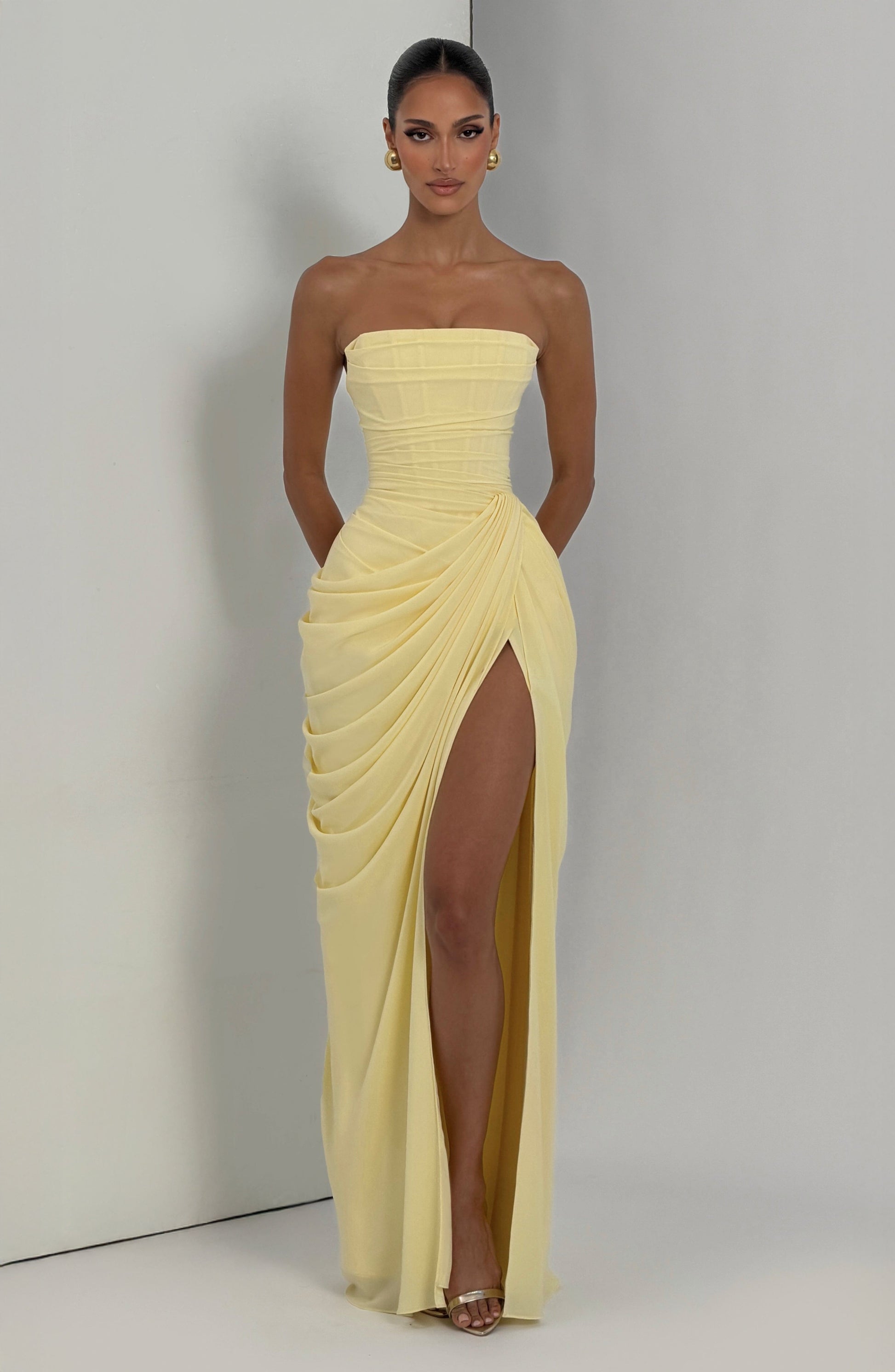 Pale yellow strapless draped maxi dress in natural lighting, showing fitted bodice and thigh slit