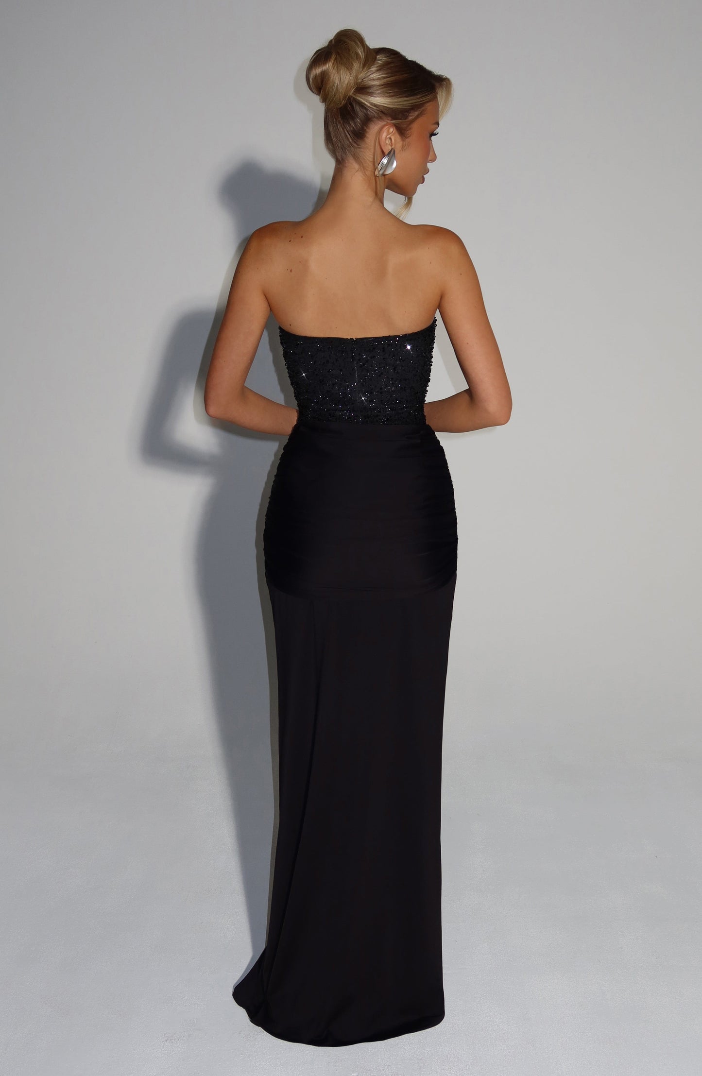 Back view of black strapless sequin corset maxi dress with straight neckline and smooth floor-length skirt