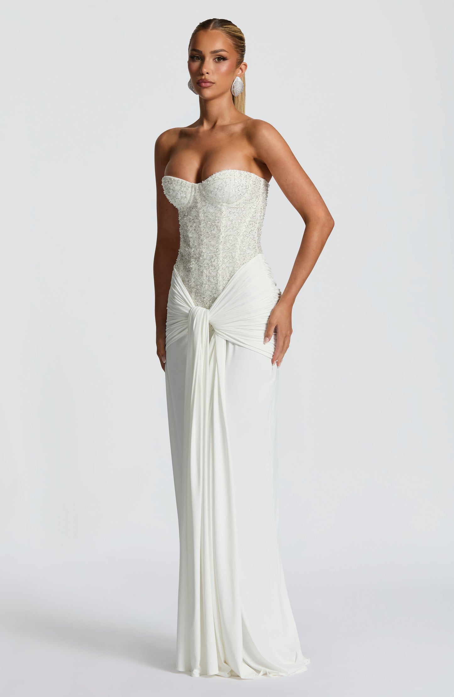 Angle view of white formal strapless sequin corset maxi dress with draped knot skirt and train