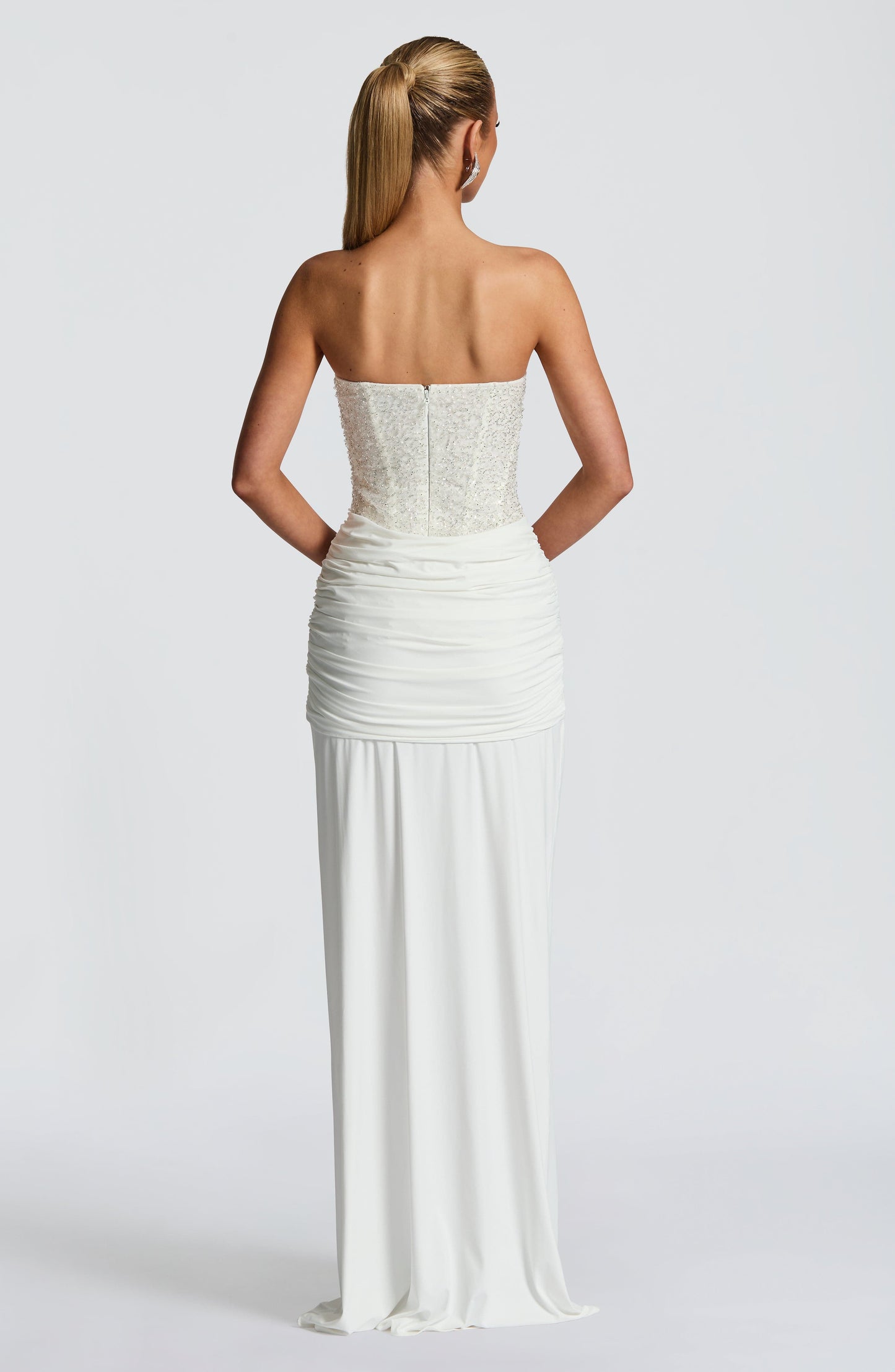 Back view of white strapless sequin corset maxi dress showing straight neckline, zipper, and ruched skirt