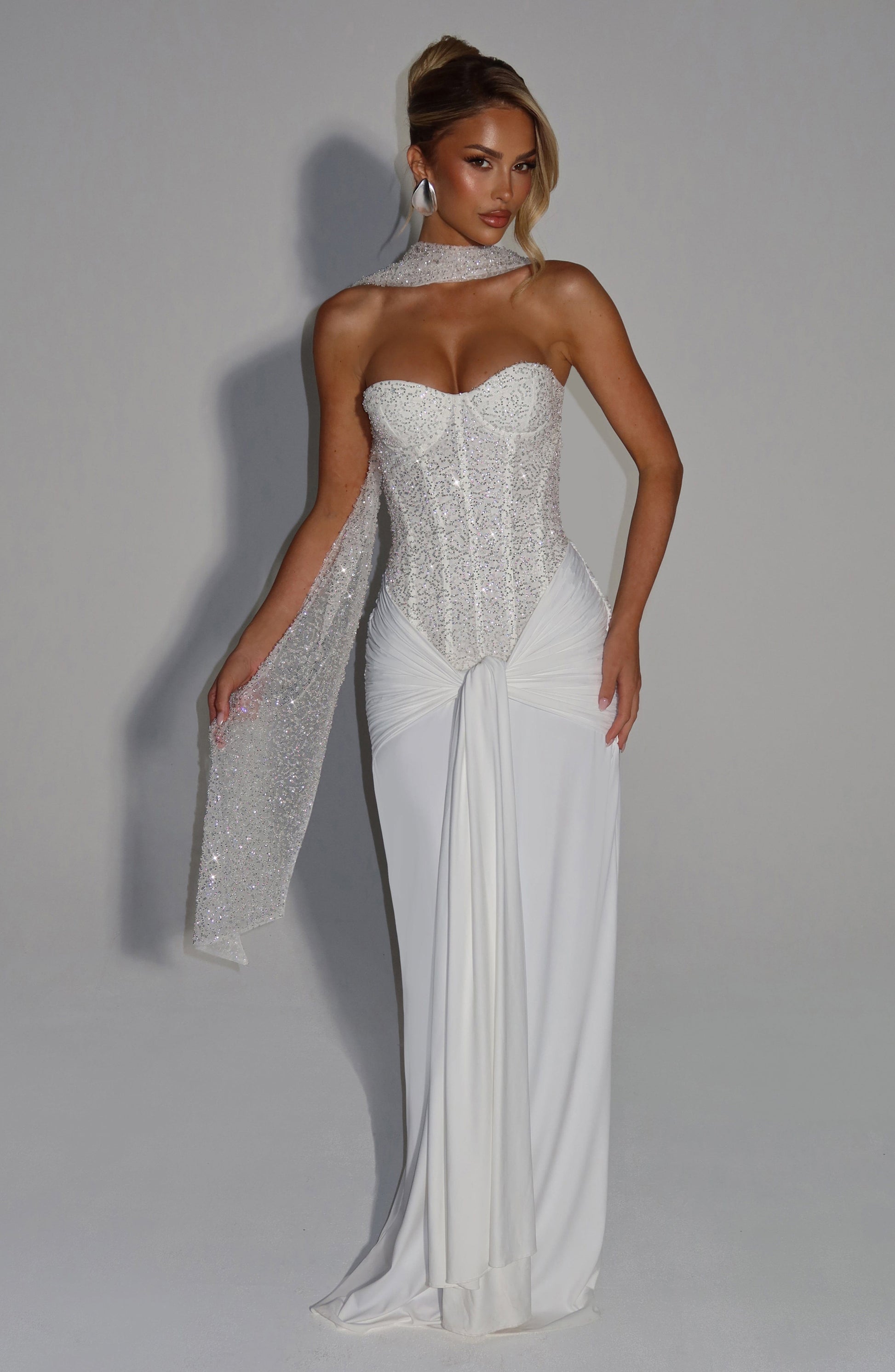 White strapless sequin corset maxi dress styled with glitter scarf wrap at neck and long draped tail