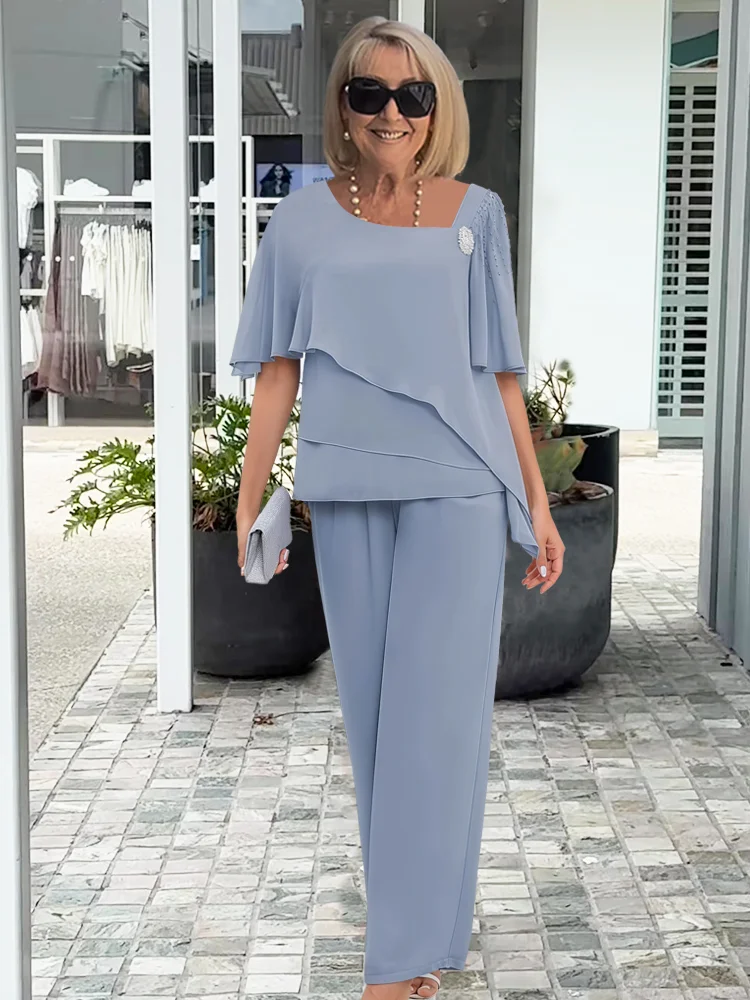 Smiling woman wearing a light blue formal two-piece layered top and wide-leg pants set, holding a clutch.