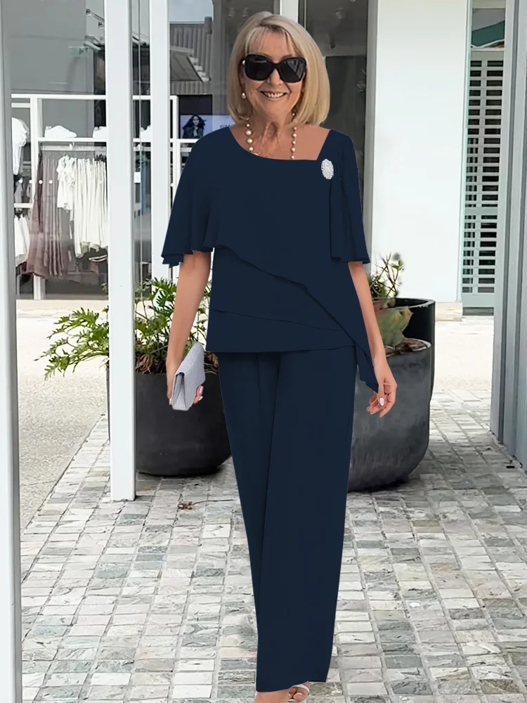Smiling woman in a dark navy formal two-piece layered top and wide-leg pants set, holding a silver clutch.