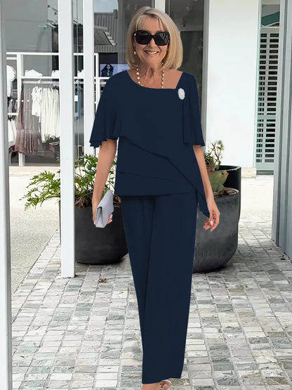 Smiling woman in a dark navy formal two-piece layered top and wide-leg pants set, holding a silver clutch.