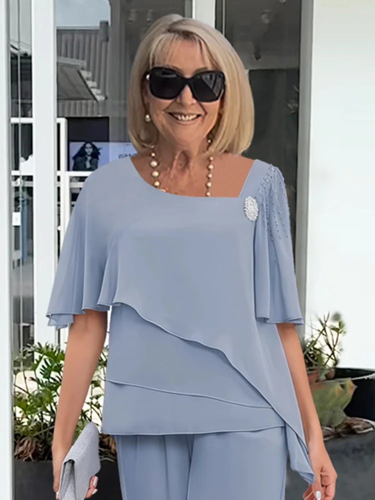 Close-up of a woman in a light blue formal layered top with a square neckline and embellished shoulder.