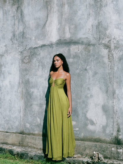 Women's olive green gathered bust keyhole maxi dress with spaghetti straps, standing against a textured concrete wall.